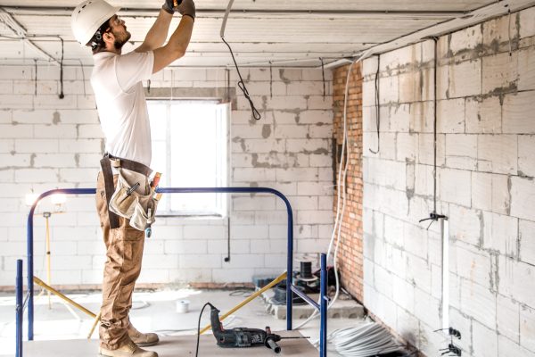 Electrician installer with a tool in his hands, working with cable on the construction site. Repair and handyman concept. House and house reconstruction.
