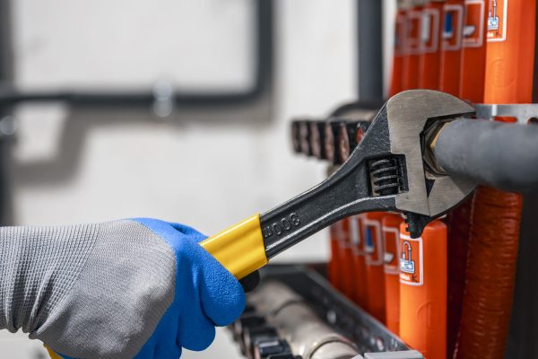 Male hands with a wrench turning off valves. Adjusting heating valves in a residential building. A plumbing and heating technician works.